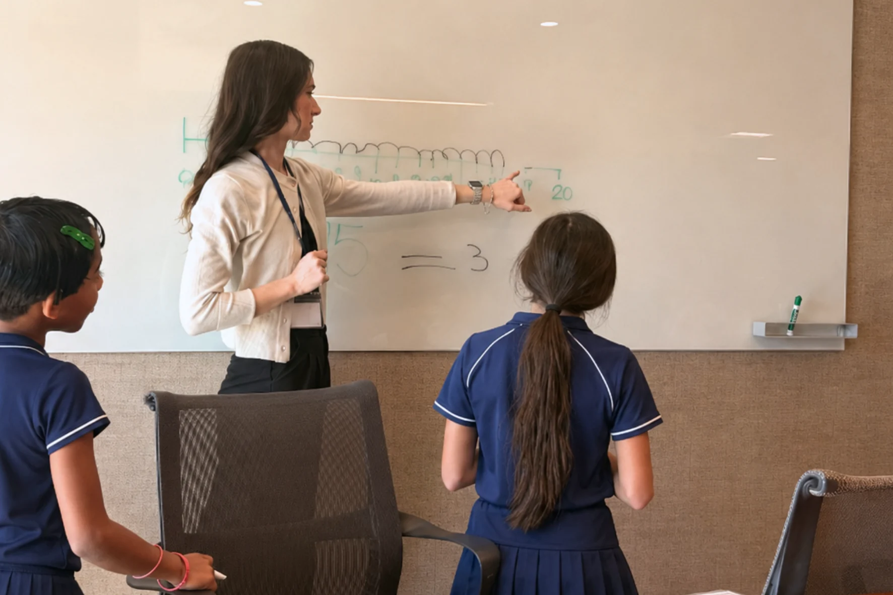 An educator explains a math problem at a whiteboard with two students.